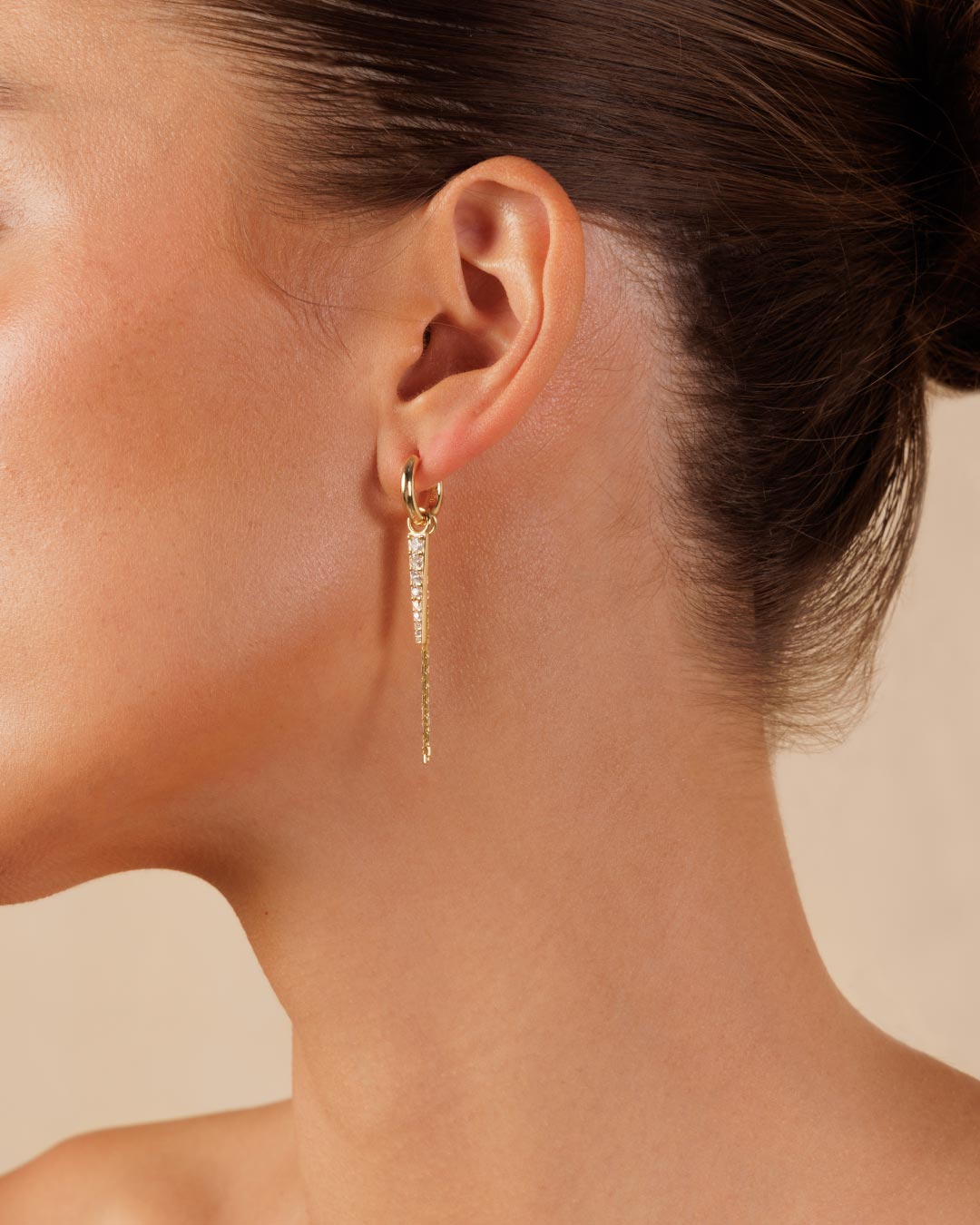 photo of a model wearing gold huggy earrings with a chain drop and gemstone charm by Camóre